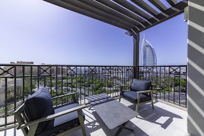 Ein Balkon mit zwei Stühlen und einem Tisch, der auf einen Stadtblick mit einem markanten Gebäude blickt.