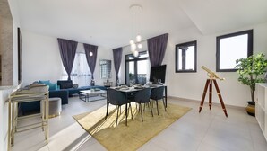 A modern living room with a dining area, a sofa set, a coffee table, and a large window with curtains. - Maison Privee - Exclusive Luxury 3BR Apt with scenic views of Burj Al Arab (Dubai)