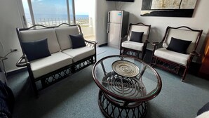 A balcony with a sofa and chairs, a refrigerator, and a flat-screen TV.
