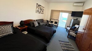 A hotel room with two beds, a sofa, a TV, and a balcony with a view.