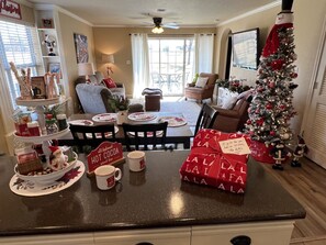 A cozy living room with a fireplace, a Christmas tree, and a kitchen area with a coffee station.