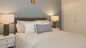 Une chambre à coucher avec une tête de lit capitonnée, un élément décoratif en forme de soleil fixé au mur, deux lampes de chevet, une porte blanche et un grand lustre.