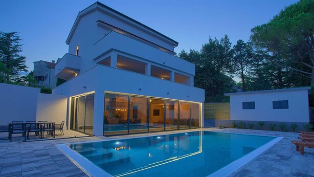 Una casa moderna de dos pisos con piscina, puertas de vidrio y un patio.
