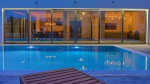 Un área de piscina moderna con paredes de vidrio, una terraza de madera y vista despejada al interior.