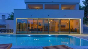 Una casa moderna con piscina, puertas de cristal y mobiliario de exterior.