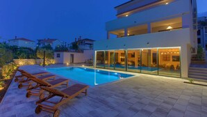 Una casa moderna de dos pisos con piscina, mobiliario exterior y un interior bien iluminado.