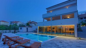 Una casa moderna de dos pisos con piscina, mobiliario exterior y un interior bien iluminado.