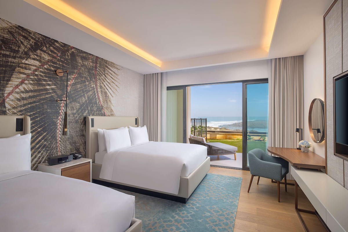 A hotel room with a large bed, a desk, a chair, a TV, and a balcony with a view.