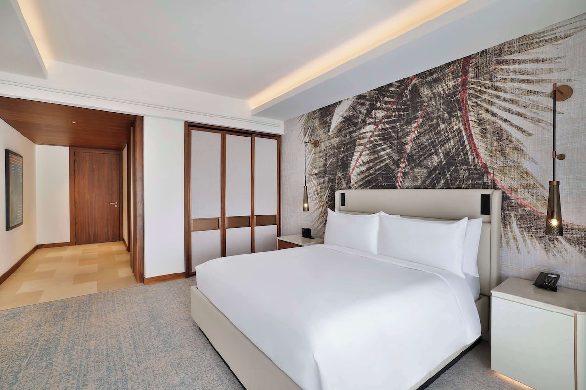 A hotel room with a large bed, a nightstand, a wall-mounted lamp, and a sliding door closet.