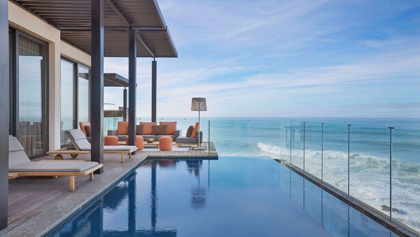 An infinity pool with a view of the ocean, modern outdoor seating, and large windows. - Conrad Rabat Arzana (Harhoura)