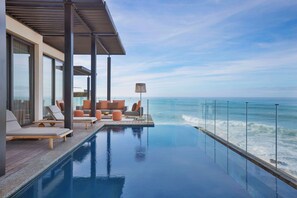 An infinity pool with a view of the ocean, modern outdoor seating, and large windows.