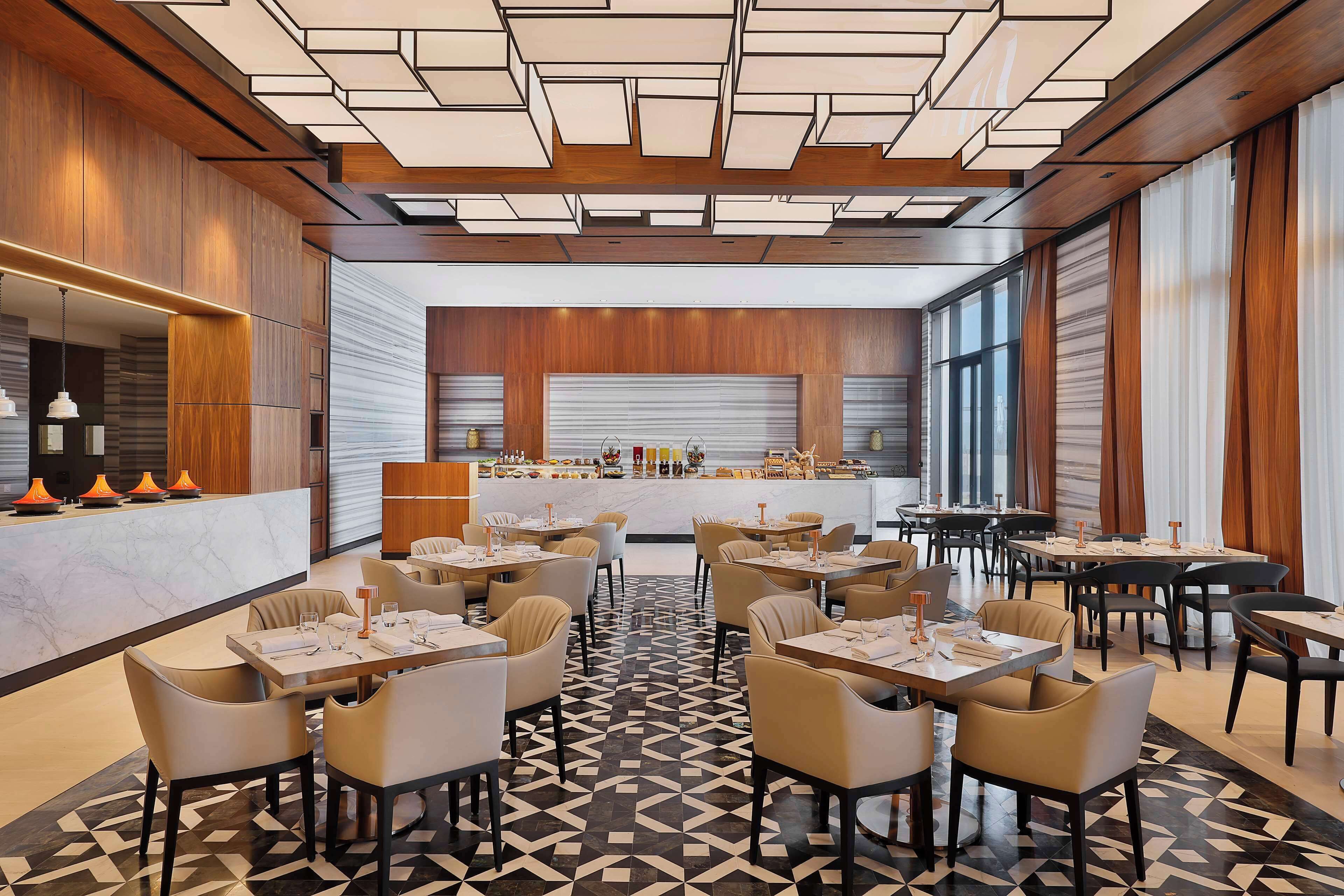 A modern restaurant with a geometric patterned floor, wooden panel walls, and a central bar area.