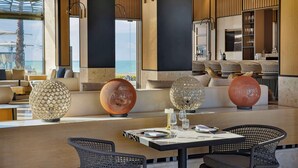 A modern dining area with a view of the sea, featuring large decorative globes, wicker chairs, and a wooden ceiling. - Conrad Rabat Arzana (Harhoura)