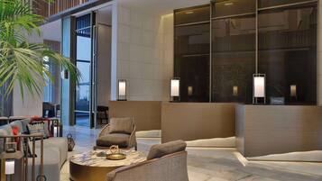 A modern hotel lobby with a reception desk, seating area, and large windows.