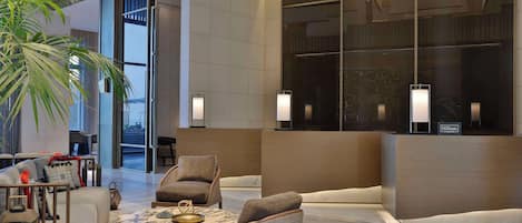 A modern hotel lobby with a reception desk, seating area, and large windows.