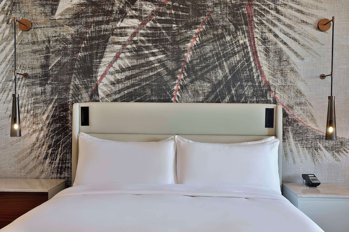 A neatly made bed with white linens, a headboard, and a nightstand with a lamp and a phone.