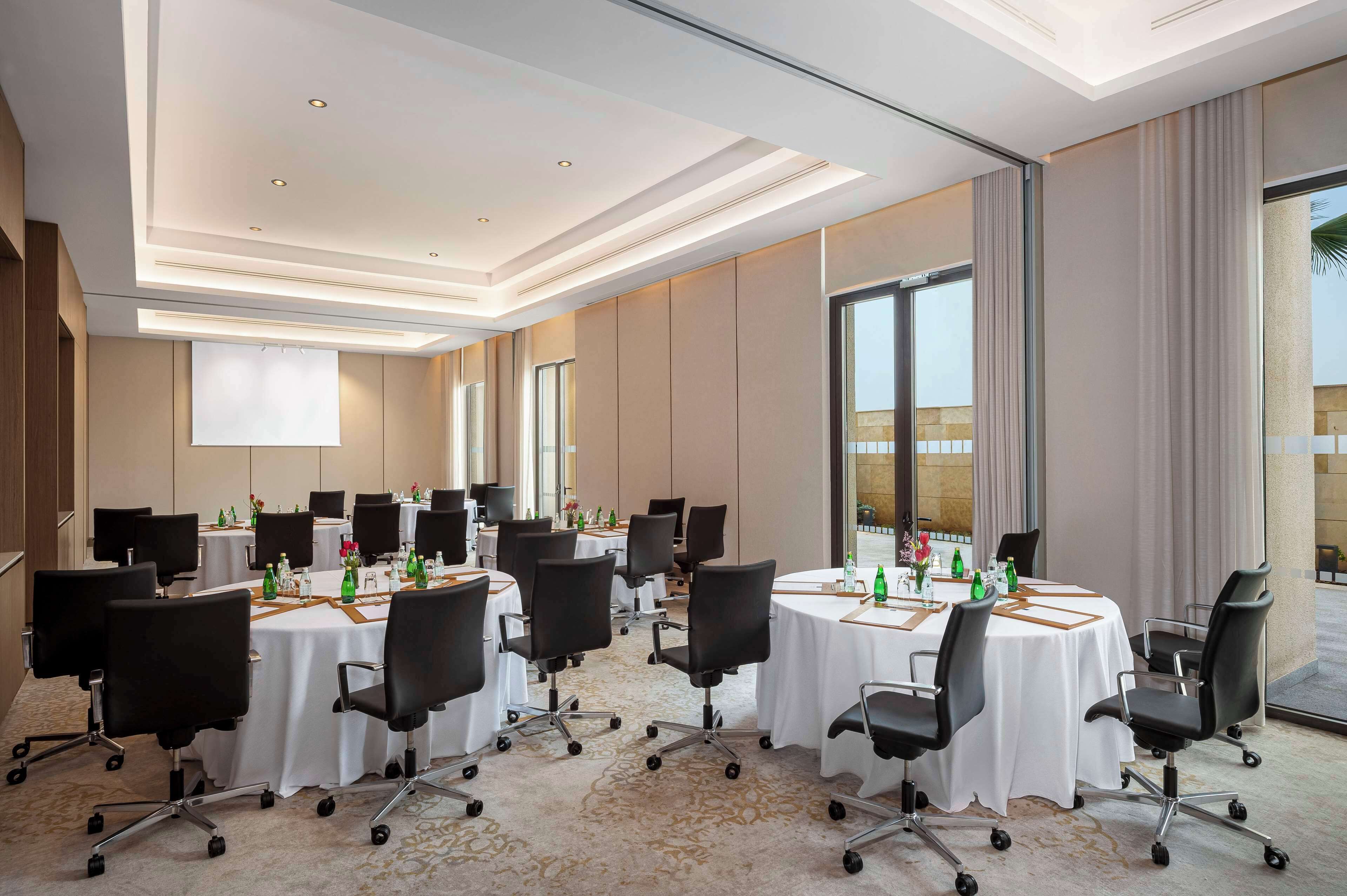 A conference room with multiple tables, chairs, and a large window providing a view of the outdoors.
