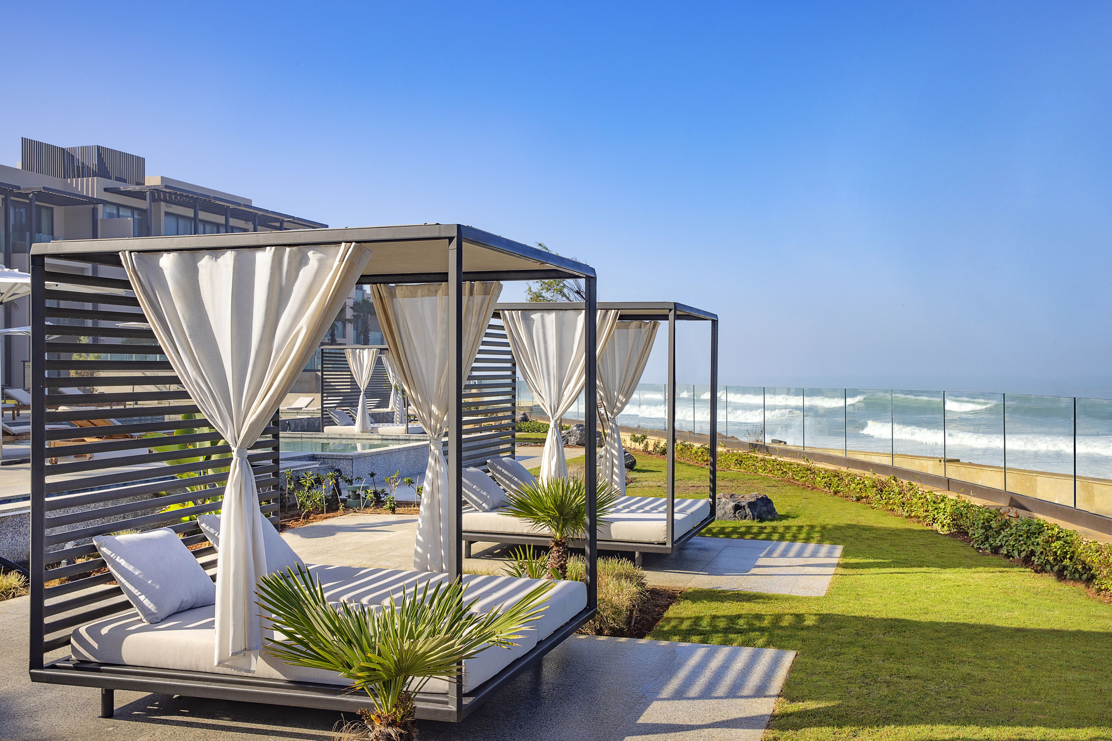 A seaside resort with outdoor seating areas featuring white canopies and cushioned loungers.