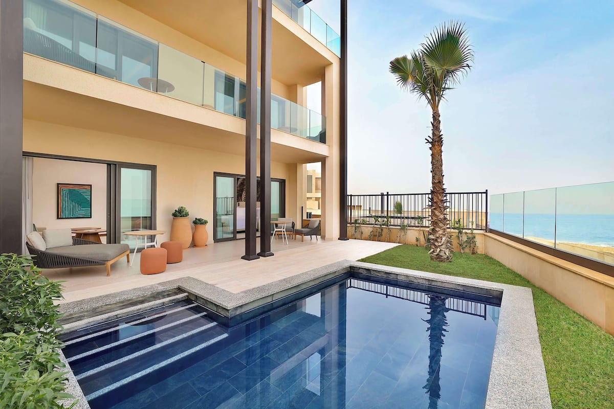 A modern hotel with a rooftop pool, outdoor seating, and a view of the ocean.