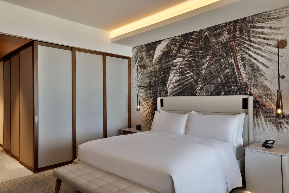 A hotel room with a large bed, a bedside table with a phone, and a wall with a leaf pattern.