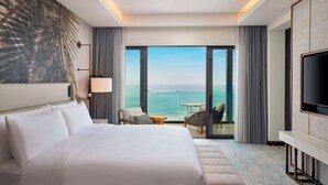 A hotel room with a large bed, a TV, a desk, and a view of the ocean. - Conrad Rabat Arzana (Harhoura)
