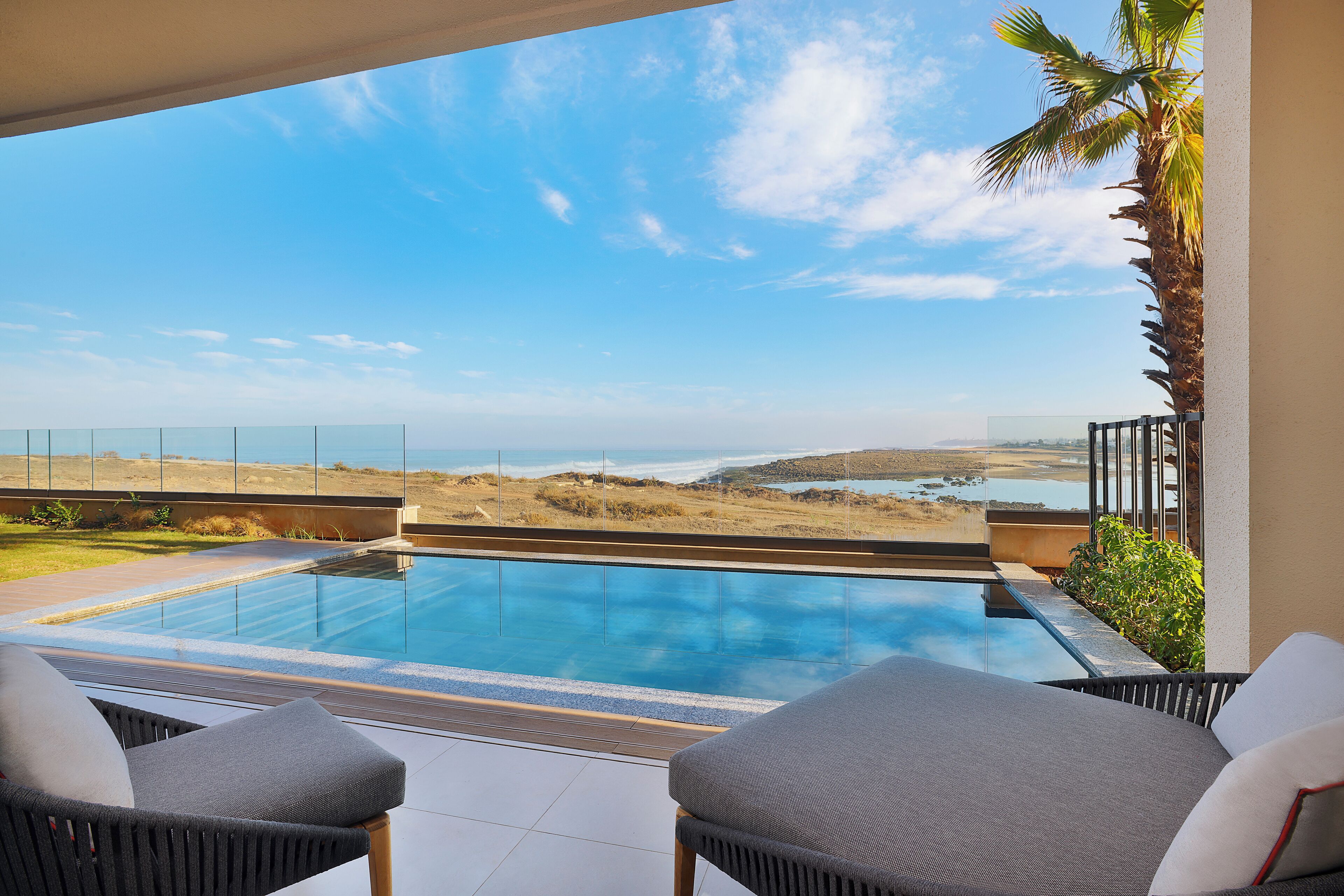 A modern outdoor pool area with a clear view of the ocean and hills.