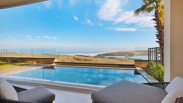 A modern outdoor pool area with a clear view of the ocean and hills.