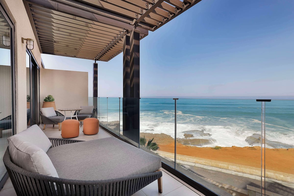 A balcony with a view of the ocean, wicker furniture, and a glass railing.