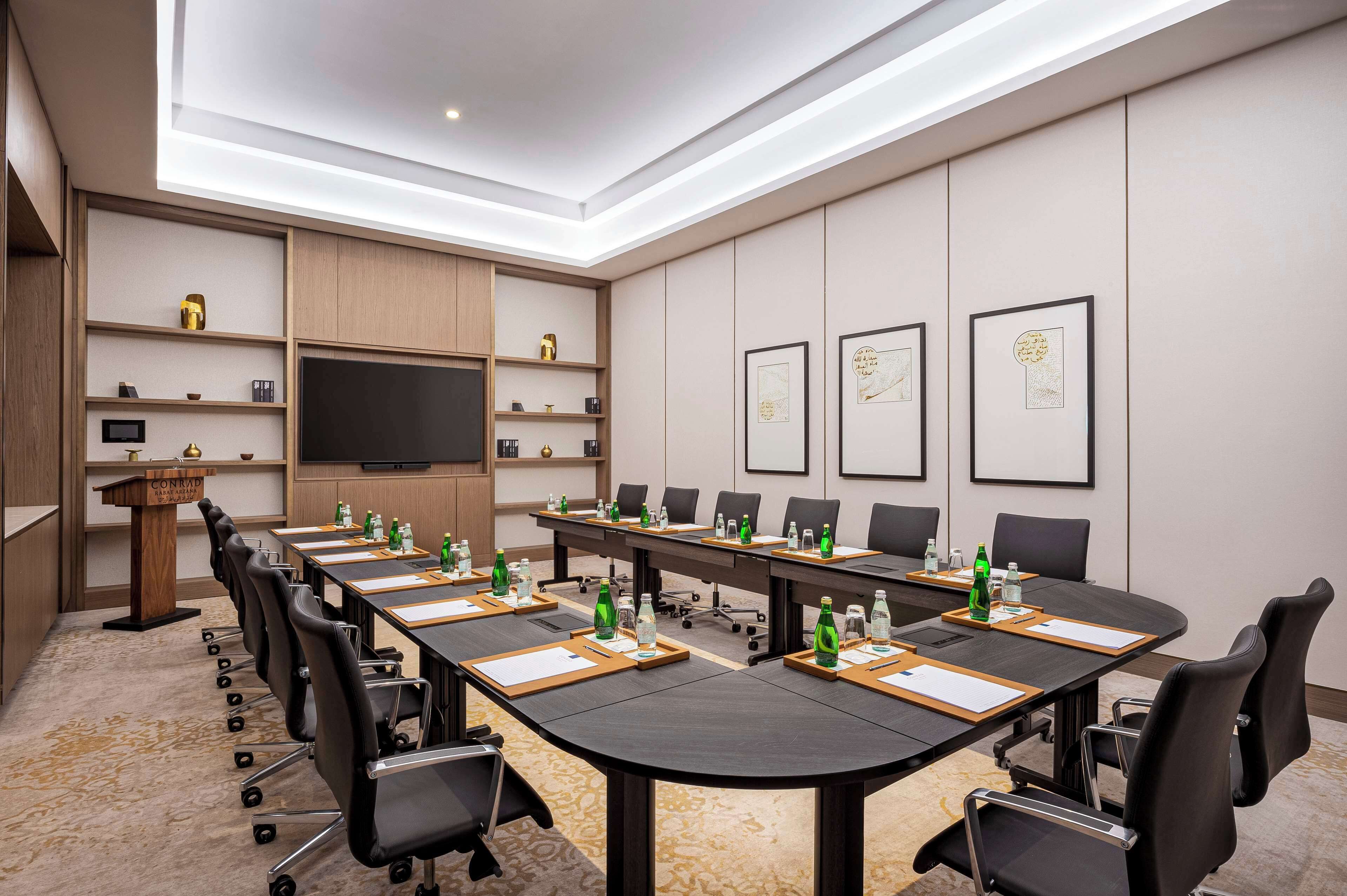 A conference room with a long table, chairs, a podium, and framed artwork on the walls.
