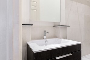 A modern bathroom with a white sink, dark cabinetry, and a large mirror above the sink.