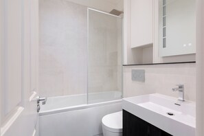 A modern bathroom with a glass shower enclosure, a white bathtub, a white sink, and a toilet.