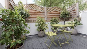 An outdoor patio area with a wooden lattice fence, potted plants, and a yellow folding table with chairs. - Elegant 2 bedrooms apt in Chelsea with patio (London)