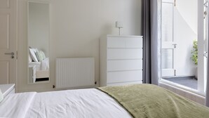 A bedroom with a bed, a dresser, a radiator, a window with curtains, and a door. - Elegant 2 bedrooms apt in Chelsea with patio (London)