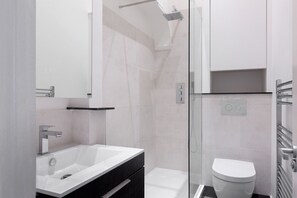 A modern bathroom with a glass-enclosed shower, a white sink, and a toilet.