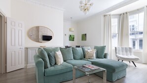 A modern living room with a green sofa, a glass coffee table, and a white armchair. - Elegant 2 bedrooms apt in Chelsea with patio (London)