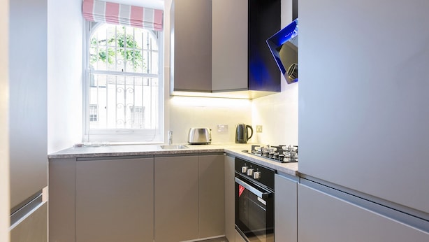 A compact kitchen with a window, a gas stove, and a built-in oven. - Elegant 2 bedrooms apt in Chelsea with patio (London)