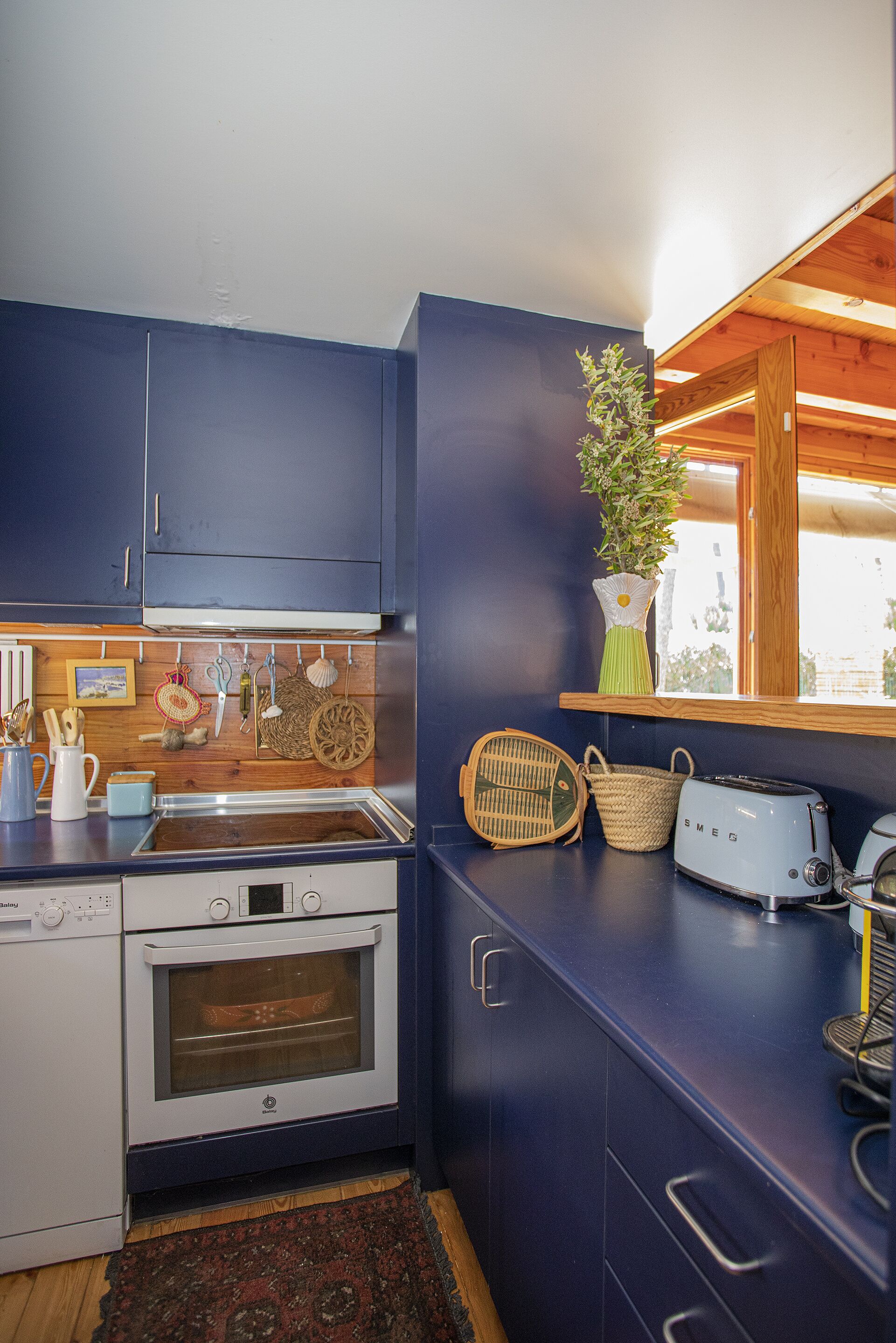 A kitchen with dark blue cabinets, a white oven, a toaster, and a window with a wooden frame.