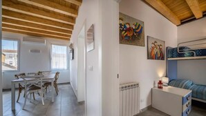 A room with a bunk bed, a dining area with a table and chairs, and a radiator. - Modern beach apartment with parking space (Chioggia)
