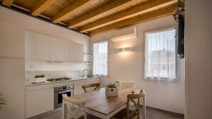 A modern kitchen with white cabinets, a wooden dining table, and a window with sheer curtains. - Modern beach apartment with parking space (Chioggia)