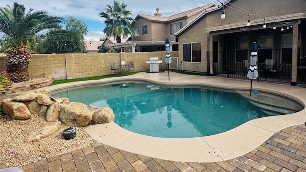 Piscina com um terraço de tijolos, área de estar externa e espaço coberto com guarda-sóis.