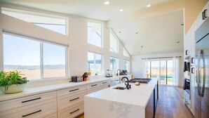 A modern kitchen with a large island, white cabinetry, and a view of the beach.
