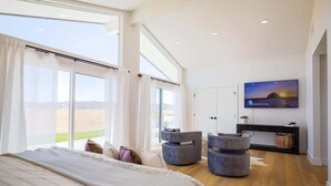A modern bedroom with a large bed, a TV, and a view of the countryside.