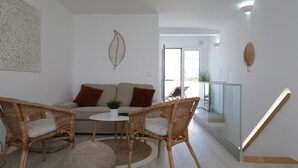 Un salon moderne avec un canapé, deux fauteuils en osier, une petite table et des œuvres d’art décoratives accrochées au mur.