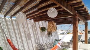 Un hamac sous une pergola en bois, agrémenté de rideaux blancs et de lanternes suspendues, d’où l’on peut admirer la vue sur la ville.