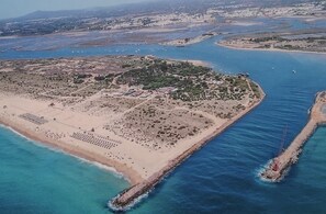 An aerial view of a coastal area with a sandy beach, a small island, and a pier extending into the water.