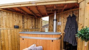 Een houten sauna met een bank en handdoeken, een whirlpool en een schoorsteen.