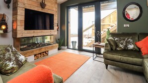 Een woonkamer met een open haard, een groene bank en een groot raam.