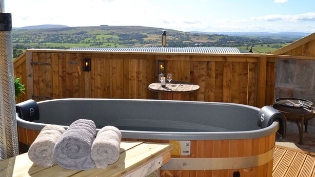 Een houten terras met een jacuzzi, handdoeken en een tafel met glazen.