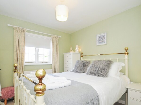 A neatly made bed with a white and grey duvet, a gold-framed headboard, and a white nightstand beside it.