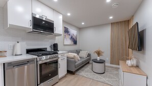 A modern kitchen with stainless steel appliances, a grey sofa, and a wooden accent wall.